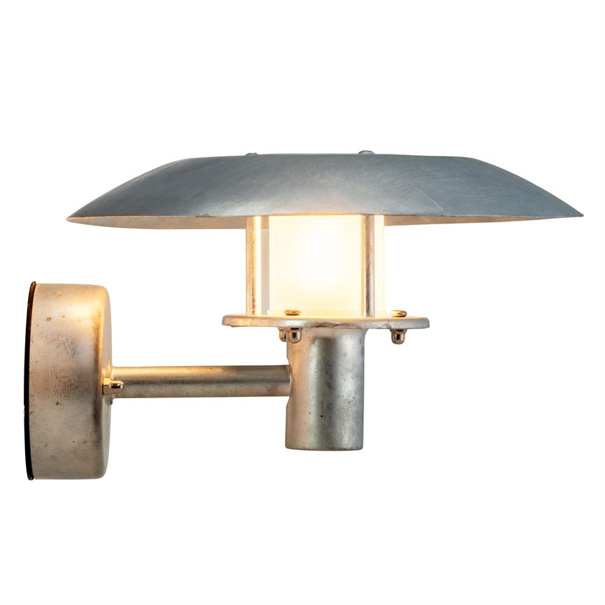Væglampe: aluminiumsk lampe lyser blødt fra en indkapslet pære under en bred, flad skærm; monteret på kort arm med cylindrisk fatning og rundt vægbeslag mod hvid baggrund.