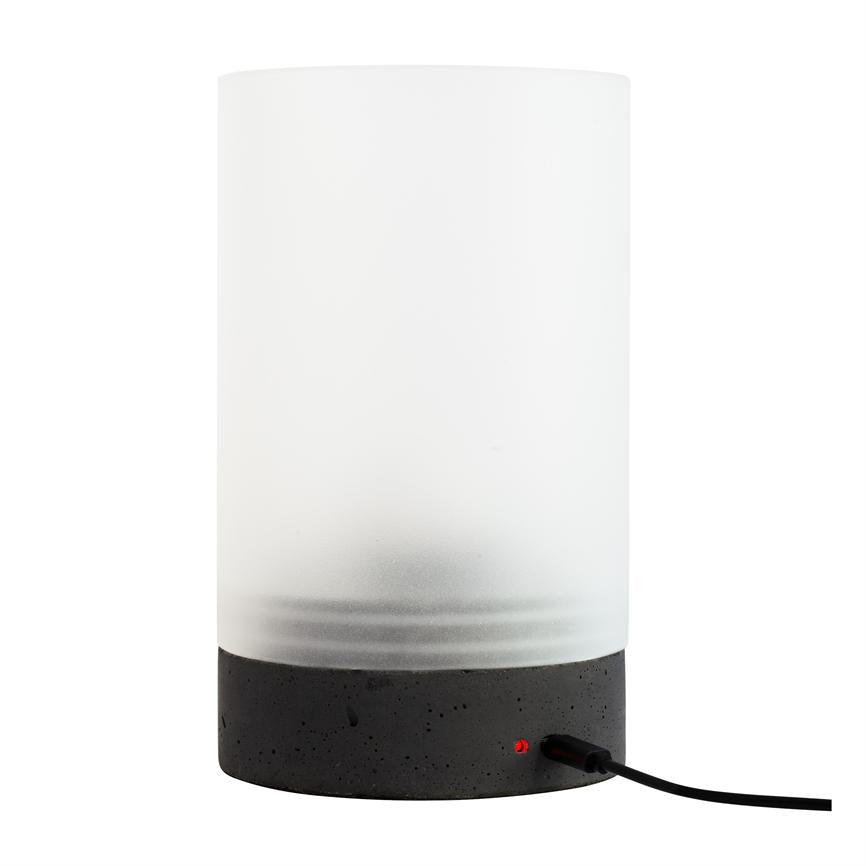 Cylindrisk bordlampe med frostet hvid glaskuppel og sort betonfod; den er tilsluttet med et sort kabel, rød LED lyser, placeret på en neutral hvid baggrund.