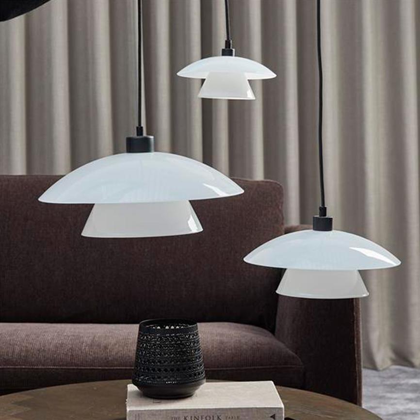 Tre hvide hængelamper svæver over et rundt bord; på bordet står en sort udskåret lysestage og en bog; i baggrunden en brun sofa foran beige gardiner. Tekst: "THE KINFOLK TABLE".