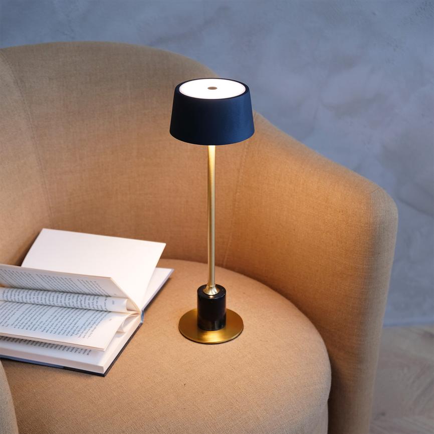Bordlampe kaster varmt lys over en åben bog, placeret på sædet af en beige polstret lænestol i et neutralt, dæmpet rum.
