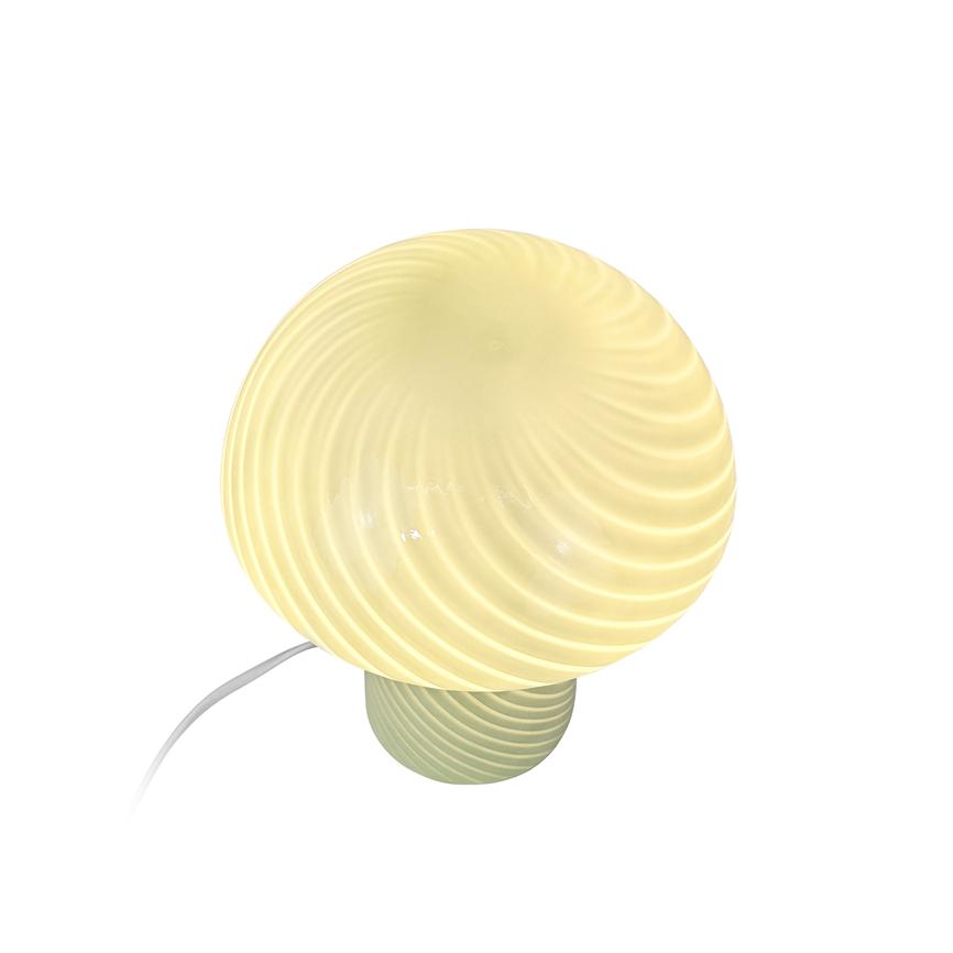 Bordlampe med rillede, kugleformet opalhvid skærm lyser blødt; monteret på kort, rillede fod, hvidt strømkabel løber til venstre mod ren, hvid baggrund.