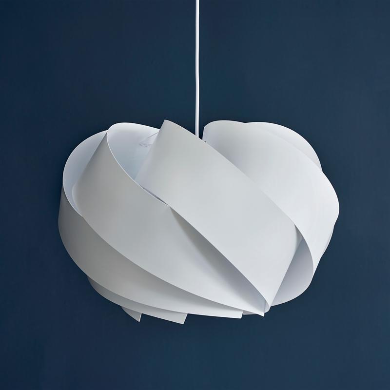 Hvid skærmlampe hænger fra en tynd ledning; overlappende, spiralformede plader danner en blød, skulpturel form, med en ensartet mørkeblå væg som baggrund.