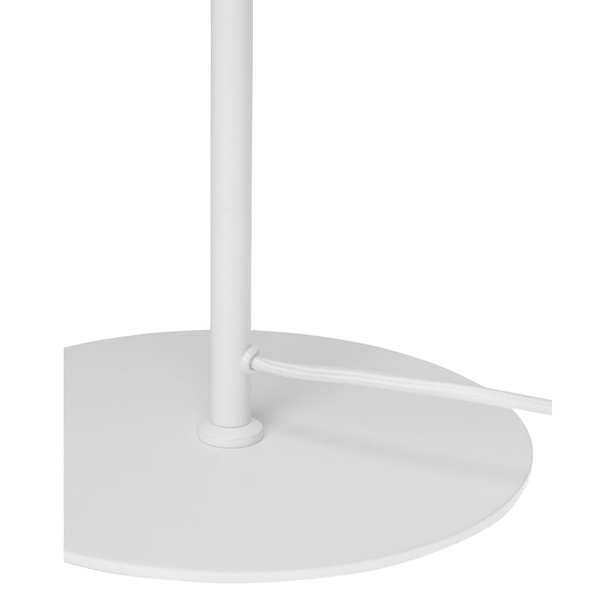 Lampens cirkulære metalfod med en lodret stang; en hvid stofbeklædt ledning føres gennem et hul i stangen. Enkel, hvid minimal baggrund.