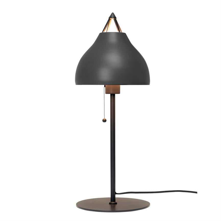 Sort/grå bordlampe står oprejst, med buet mørkegrå skærm, kobberdetaljer og hængende trækkæde; på rund metalfod med synligt kabel mod hvid baggrund.