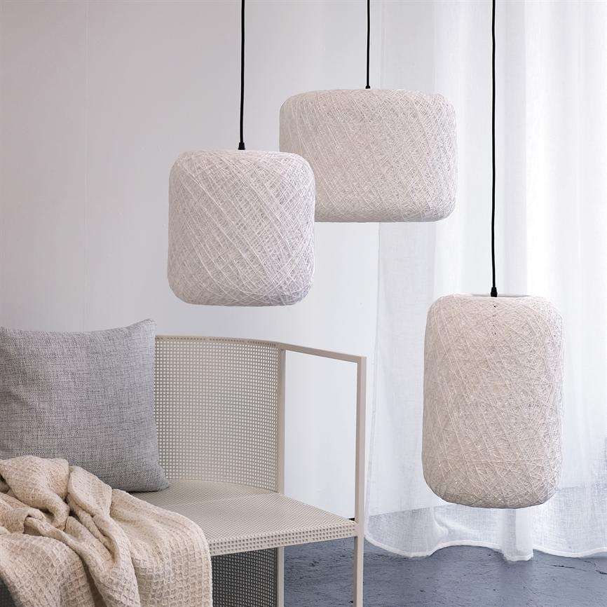 Tre hvide, snorindpakkede pendler hænger over en metalstol med grå pude og beige plaid i et lyst, minimalistisk rum foran et hvidt gardin.