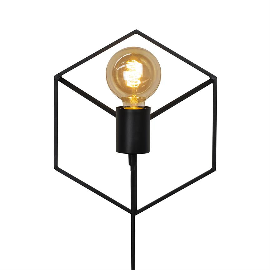 Sort metalkube-lampe udstråler en varm, tændt glødelampe; pæren sidder centralt i en åben, geometrisk ramme, med strømledning hængende ned mod hvid baggrund.