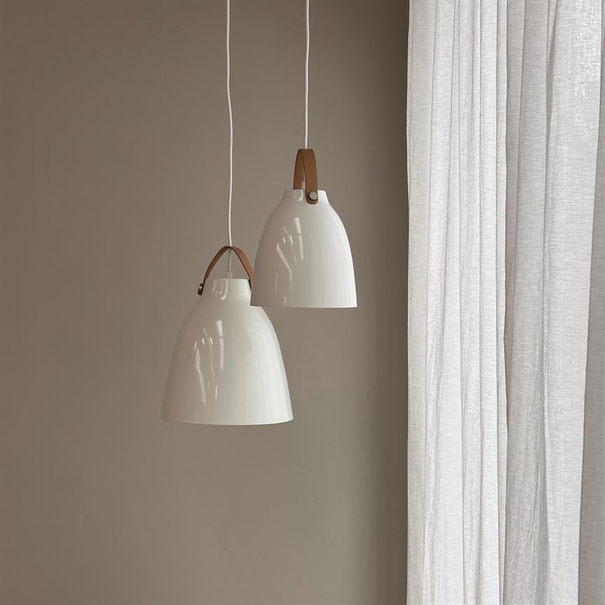 To hvide pendellamper med brune læderstroppe hænger fra loftet foran en varm beige væg, ved siden af lyse, lette hvide gardiner; den ene hænger lidt lavere og overlapper den anden.