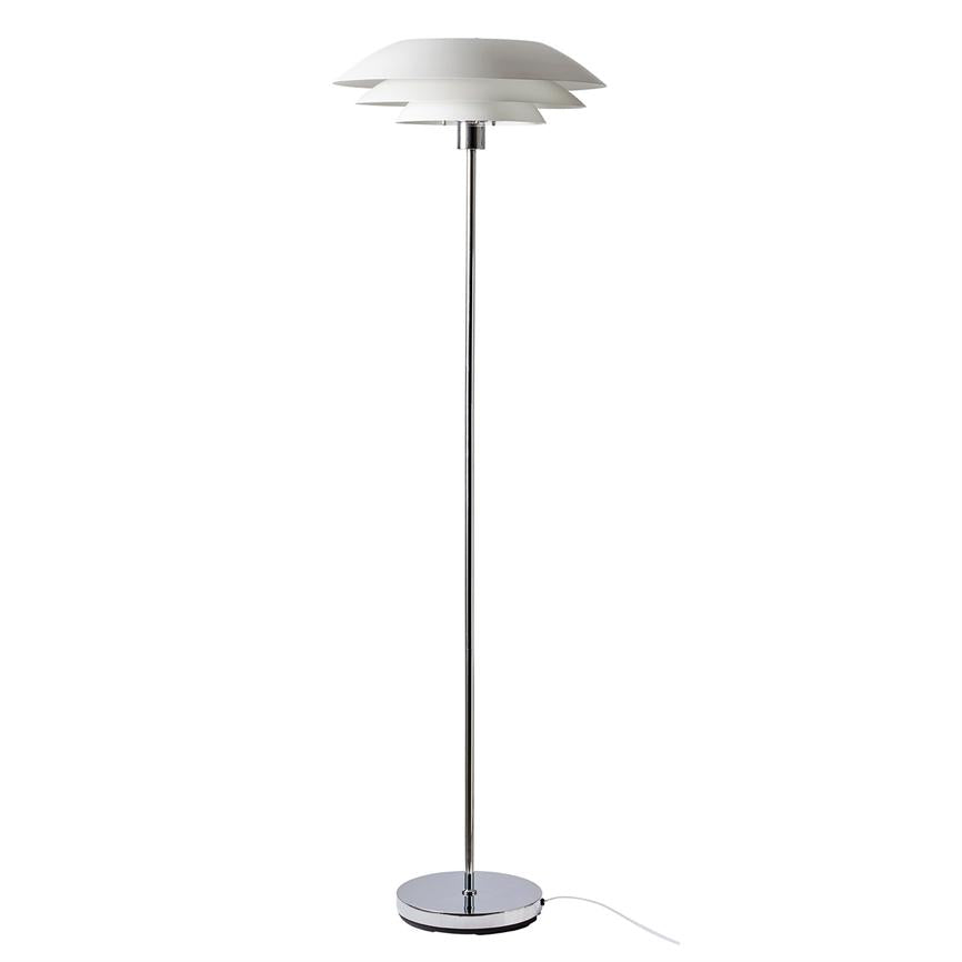 Gulvlampe med lagdelte, hvide skærme står oprejst; den udsender blødt, nedadrettet lys; slank kromstang og rund krombase med hvid ledning mod ensfarvet hvid baggrund.