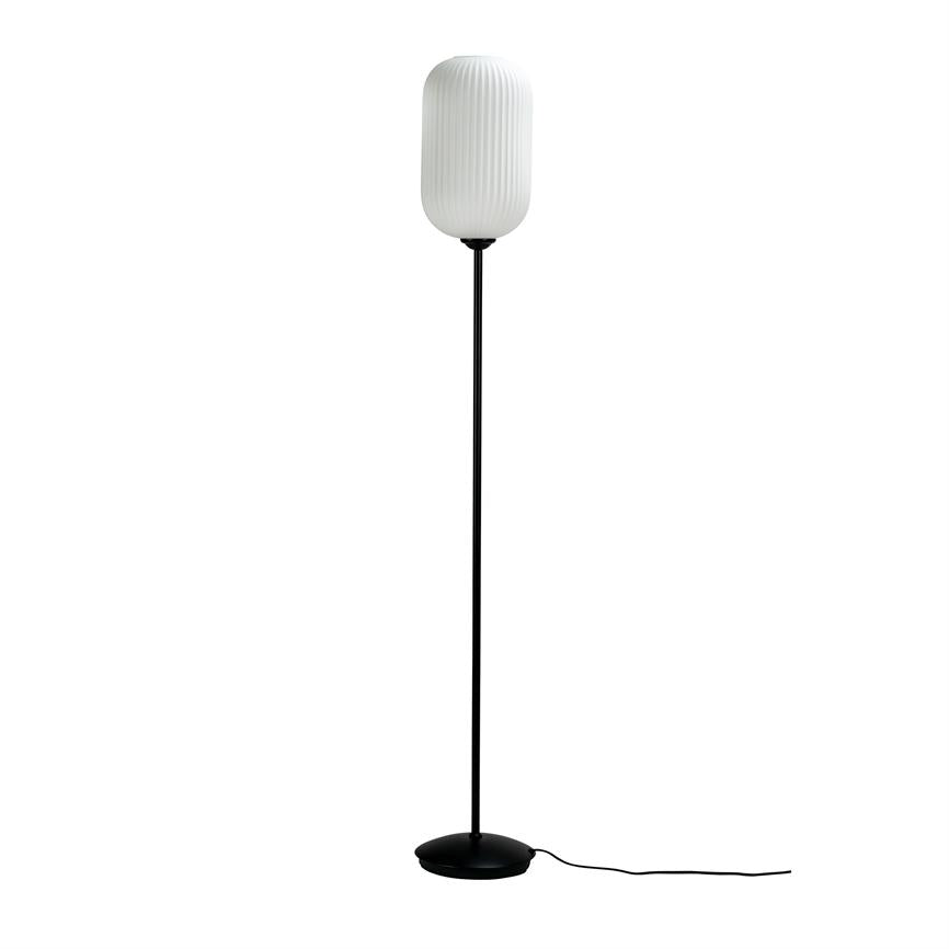Gulvlampe står oprejst mod en hvid baggrund; en slank sort stang og flad rund fod bærer en hvid, lodret rillede, oval skærm, med en løs sort ledning.