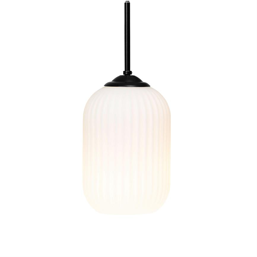 En aflang, ribbet hvid pendellampe hænger fra en sort metalstang og udsender blødt, varmt lys mod en ensartet hvid baggrund i et minimalistisk rum.
