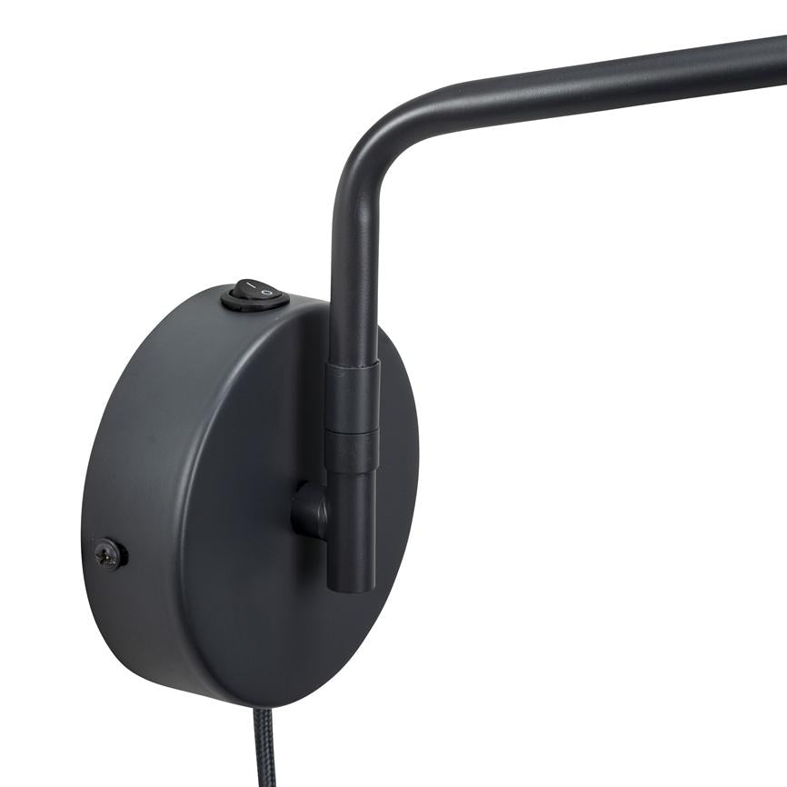 Sort, rund vægmontering til lampe holder en buet, justerbar arm; en lille vippeknap mærket "O" sidder øverst, og et stofbeklædt kabel fører nedad mod en hvid baggrund.
