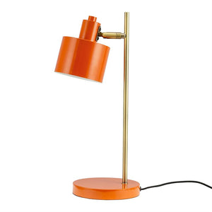 En orange metal bordlampe vipper med cylindrisk skærm nedad; den står på en rund orange fod med en slank messingstang og sort ledning mod en hvid baggrund.