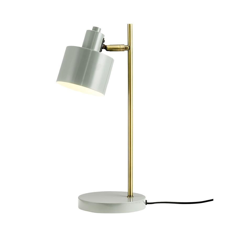 En bordlampe med grå cylinderformet skærm og messingstang; skærmen peger skråt nedad og udsender blødt lys, placeret på hvid baggrund.