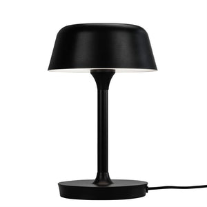 Sort bordlampe står på en rund base, med slank stang og rund, nedadvendt skærm med hvid inderside; placeret alene mod en ensartet hvid baggrund.