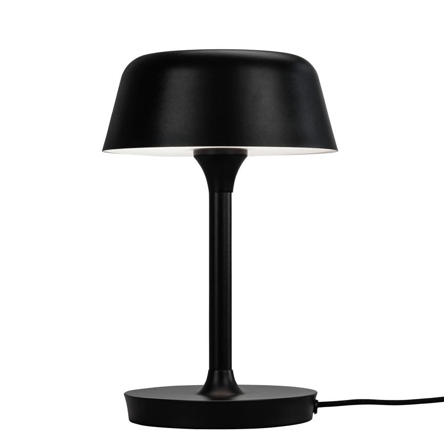 Sort bordlampe står på en rund base, med slank stang og rund, nedadvendt skærm med hvid inderside; placeret alene mod en ensartet hvid baggrund.