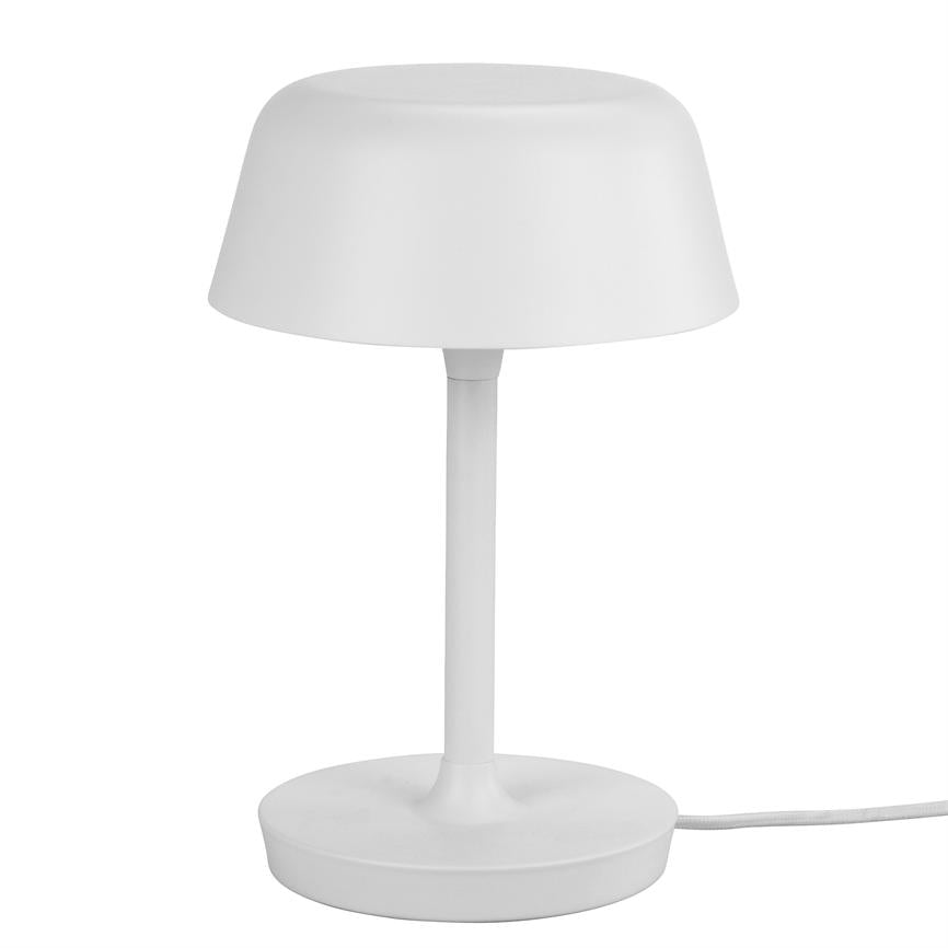 Hvid bordlampe står slukket på hvid baggrund; rund skærm og slank stang over cirkulær fod, med synlig strømledning, simpel og minimalistisk form.