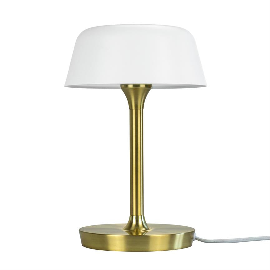 En bordlampe står med hvid skærm på en slank, børstet messingstang over en rund messingfod med synlig hvid ledning, isoleret mod hvid baggrund.