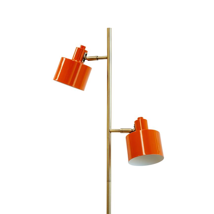 Gulvlampe har to justerbare, cylindriske orange lampeskærme monteret på en slank messingstang; skærmene er vinklet nedad mod en hvid baggrund.