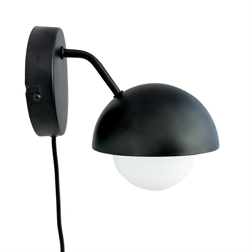 Væglampe med sort halvkugleformet skærm; buet arm holder en hvid glaskuppel. Monteret på rund vægplade med synlig sort ledning, vist mod en hvid baggrund.
