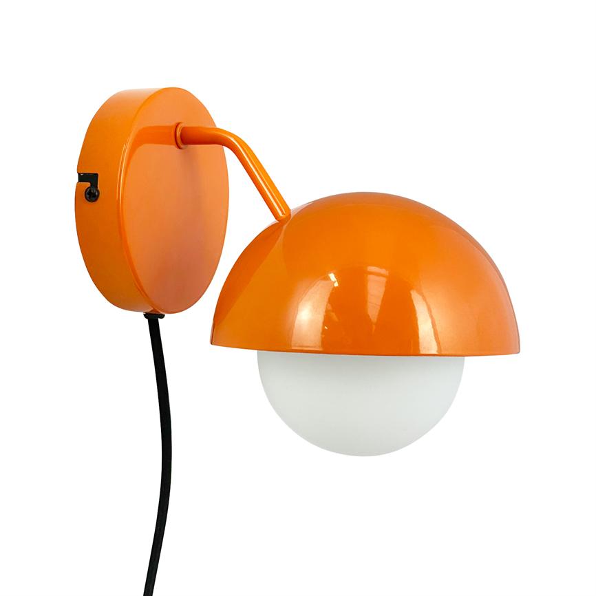 En vægmonteret orange lampe med halvkugleformet skærm dækker en hvid glaskuppel; en kort arm forbinder til rund vægplade, sort ledning hænger ned.