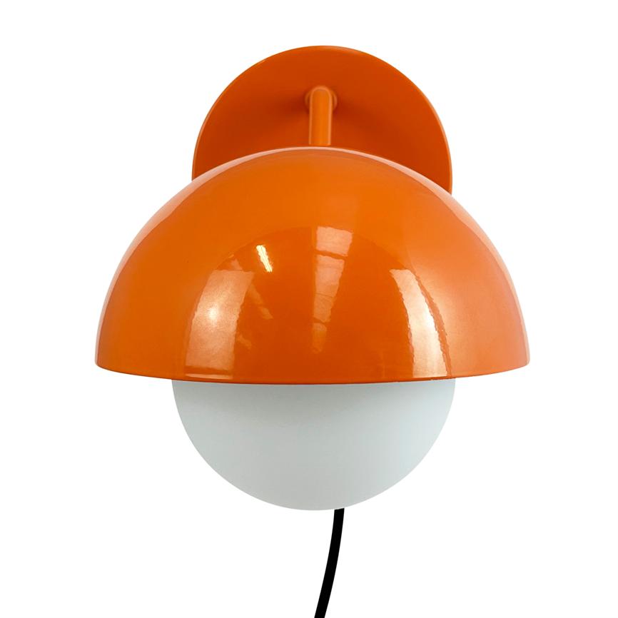 Væglampe med orange halvkugleskærm dækker en hvid glasglobus, monteret på rundt vægbeslag; sort ledning hænger ned foran en ensartet hvid baggrund.