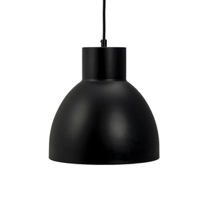 En sort metal pendellampe hænger i en tynd sort ledning; dens matte, runde kuppel afskærmer lyset nedad mod en ren, hvid baggrund i et minimalistisk udtryk.