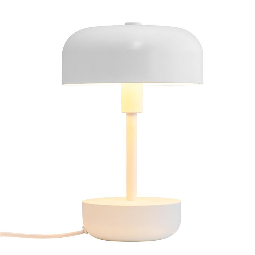 En hvid bordlampe udsender varmt lys; en slank stang forbinder en rund skålformet fod med en bred, buet skærm på en neutral hvid baggrund.