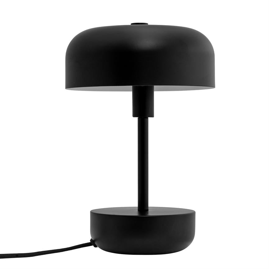 Sort bordlampe med rund skærm og cylindrisk stander, står slukket; rund base hviler på hvid baggrund, med en sort stofbeklædt ledning ud til venstre.