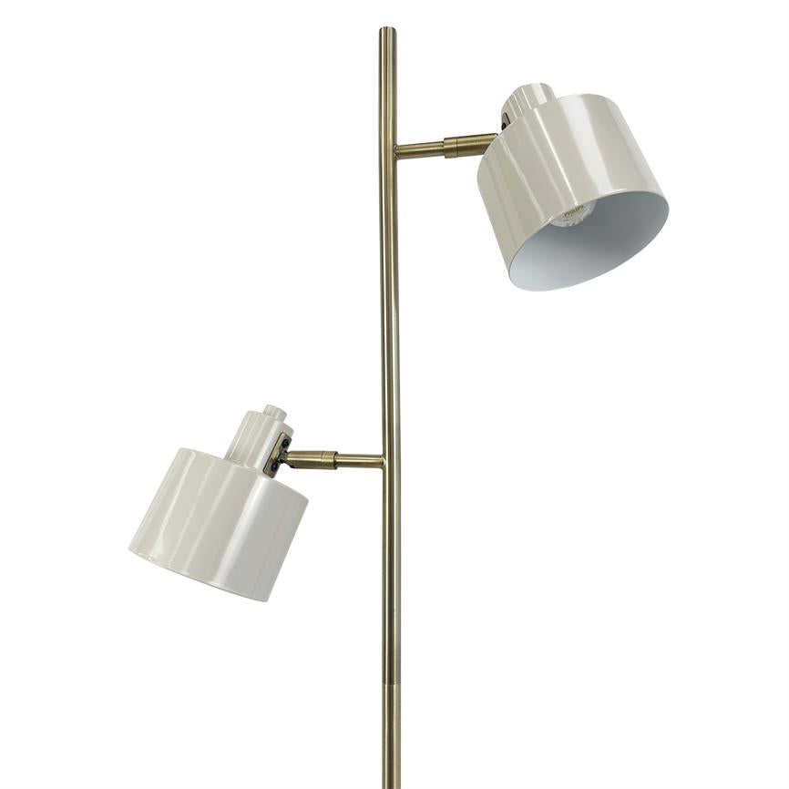 Gulvlampe med to hvide metalskærme, hver vinklet forskelligt; de er monteret på en slank antik messingstang foran en ensartet hvid baggrund.