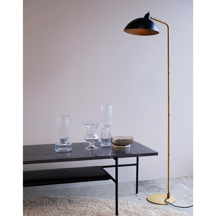 Gulvlampe i messing står ved siden af et lavt marmorbord; bordet rummer tre klare glasskåle og en lille skål, omgivet af en lys væg og et lyst, blødt tæppe.