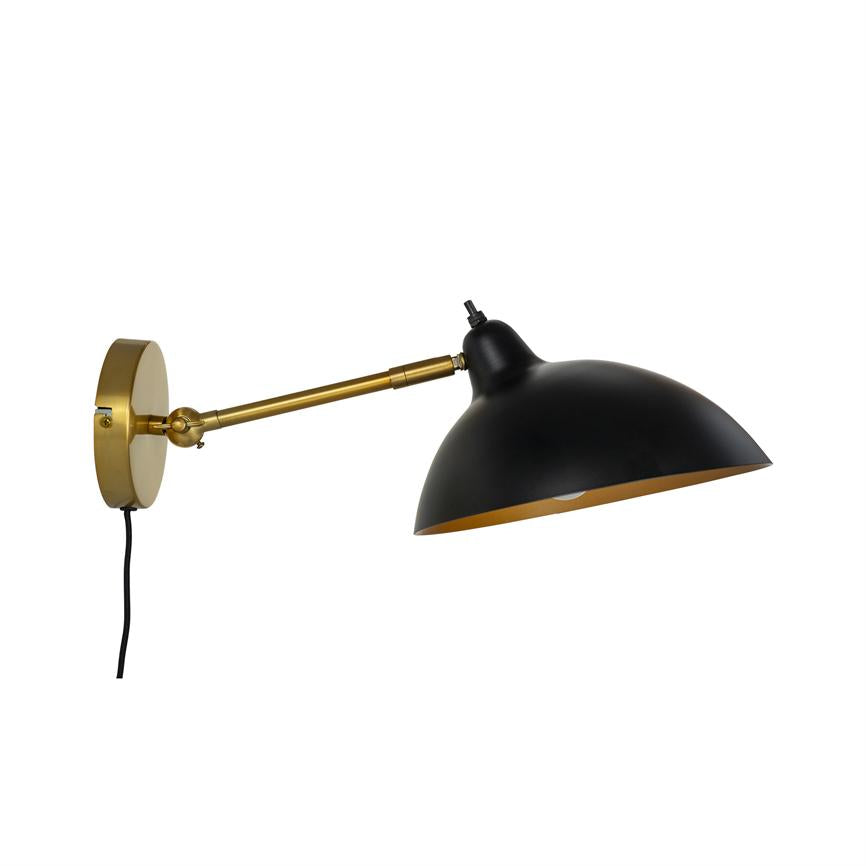 Væglampe med sort kuppelskærm og guldfarvet metalarm, monteret på et rundt vægbeslag; armen er udstrakt og skærmen vippet nedad mod en hvid, neutral baggrund.