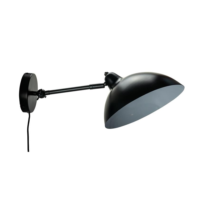 Sort væglampe med buet skærm, arm udstrakt og vinklet nedad; monteret på rundt beslag, med synlig ledning mod en neutral hvid baggrund.
