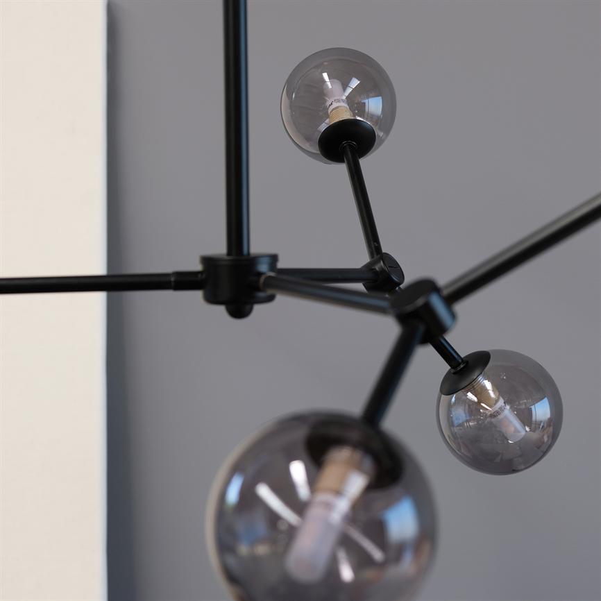 Moderne loftlampe med tre røgfarvede glaskugler, monteret på sorte metalarme, hænger fremtrædende foran en dæmpet grå væg i et minimalistisk interiør.