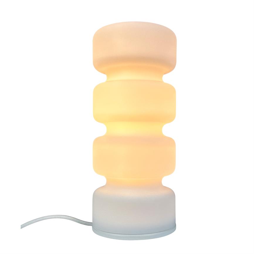 En hvid, buet bordlampe udsender varmt, diffust gult lys; fire tætsiddende runde segmenter står lodret på en rund fod med en hvid stofledning mod venstre på hvid baggrund.