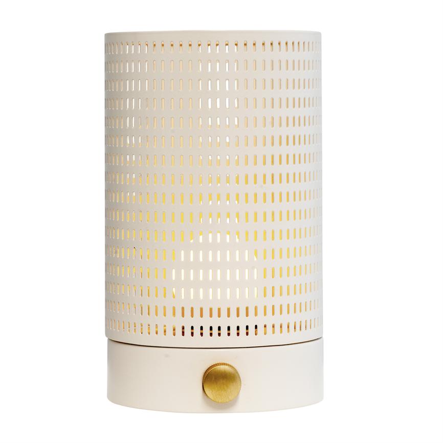 Cylindrisk bordlampe med hvid perforeret metalhylster; varmt lys skinner gennem rektangulære huller, monteret på mat hvid fod med rund, messingfarvet drejeknap, placeret mod hvid baggrund.