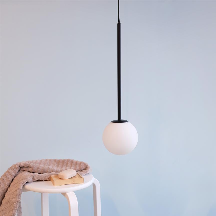 En hvid globependellampe hænger i en sort ledning; et lille hvidt bord bærer et foldet beige håndklæde og en sæbe på en trådbakke; scenen står mod en lys blå væg.