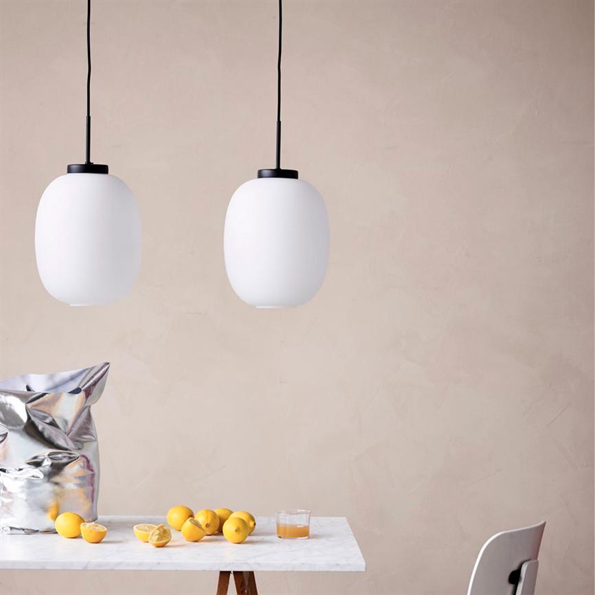 To hvide pendellamper hænger over et marmorbord, hvor gule citroner, et glas juice og en skinnende sølvpose ligger, mod en lys beige væg med en enkel stol ved bordet.