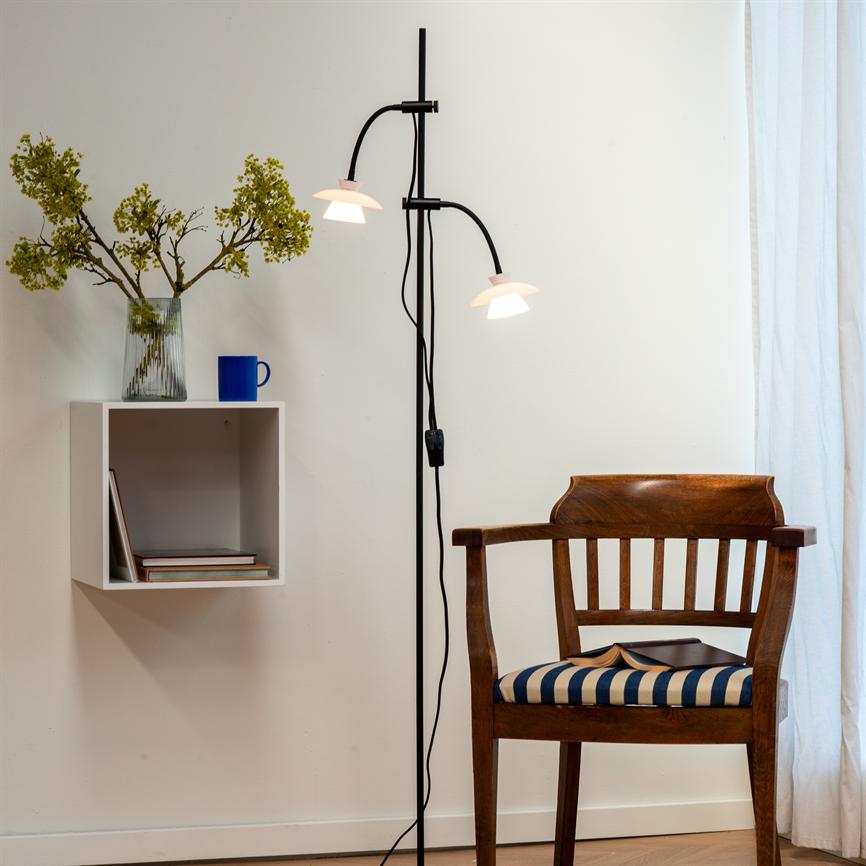 Træstol med blå-hvid stribet pude og åben bog på sædet; høj sort gulvlampe kaster lys; ved siden vægmonteret hylde med vase og blå kop i et hjørne.