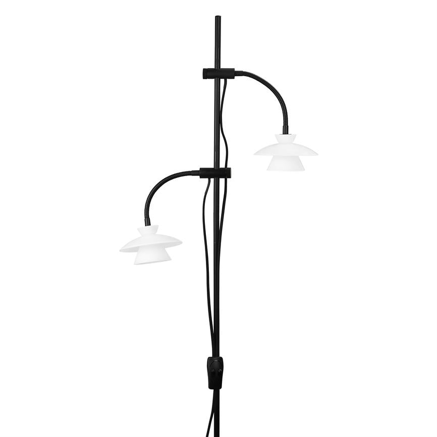 Sort stående lampe med to bøjede fleksible arme, der holder hvide dobbelte skærme; lamperne peger nedad. Lampestang med ledning og kontakt, præsenteret mod hvid baggrund.