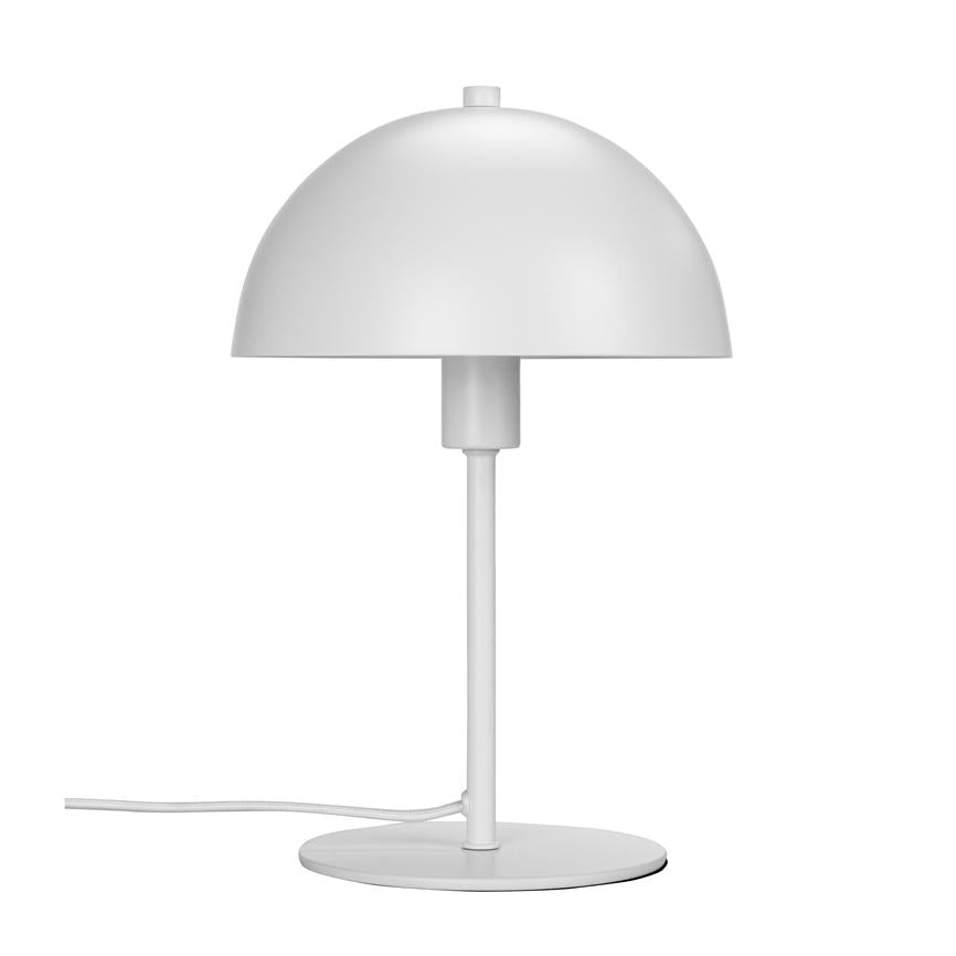 En hvid bordlampe står på en rund fod, med halvkugleformet skærm og tynd stang; ledningen ligger udstrakt, alt mod en ensartet hvid baggrund.