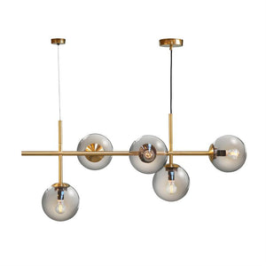 En moderne loftslampe med fem røgfarvede glasglober på en guldfarvet stang, hænger i to kabler og vises mod en ensartet hvid baggrund.