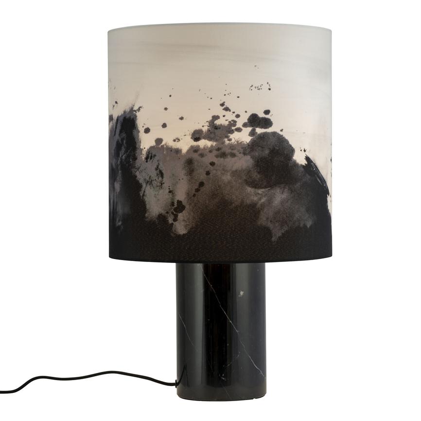 Bordlampe med cylindrisk sort marmorfod og hvid skærm, som har sorte blæk- eller akvarelpletter; står på hvid baggrund, sort ledning ligger bøjet forrest.