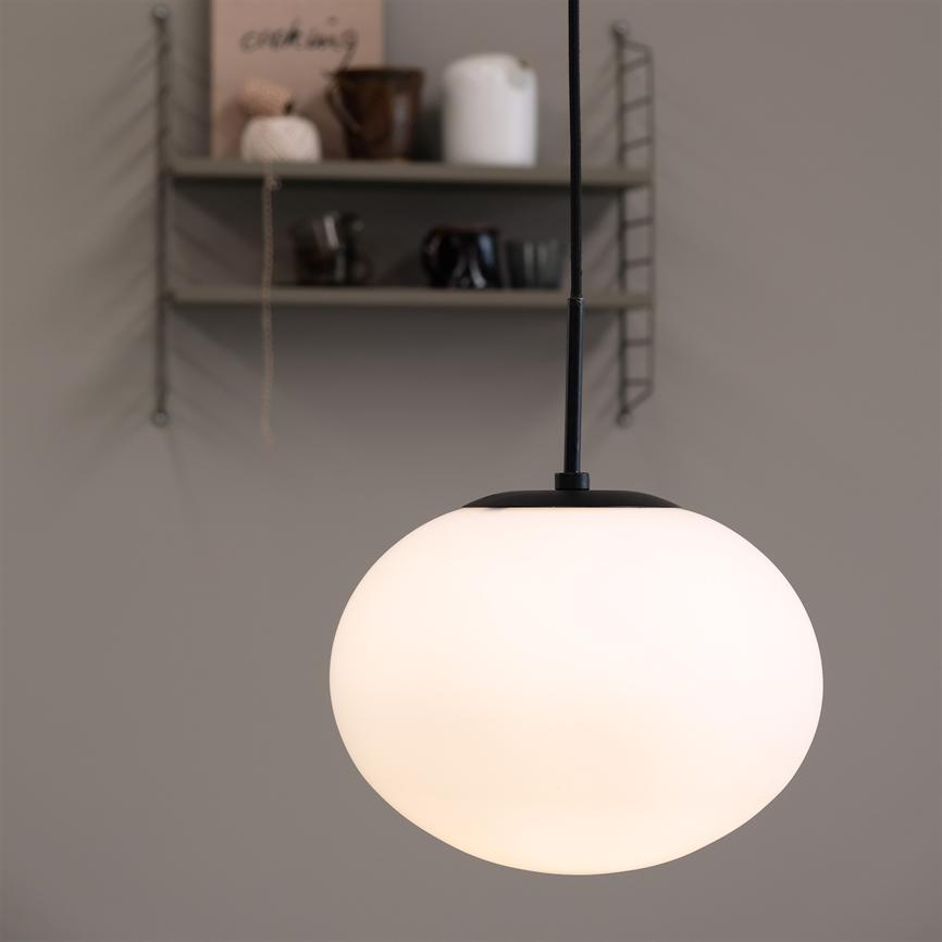 Lampen: en rund, hvid pendel, hænger tændt og kaster blødt lys; bagved væghylde med krukker, kopper og en bog med teksten "cooking".