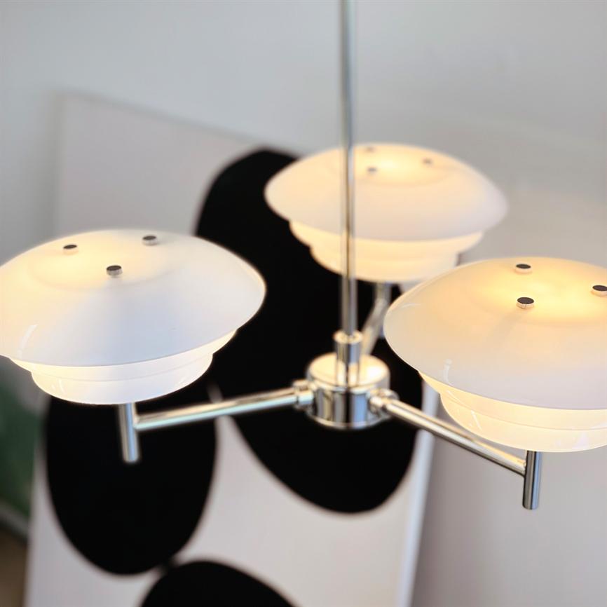 En moderne loftlampe hænger og udsender varmt, diffust lys; i baggrunden ses et sort-hvidt abstrakt maleri på væggen.