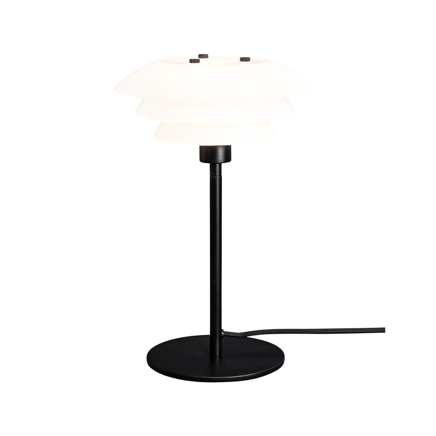 Bordlampe med lagdelt hvid skærm, der udsender blødt lys; slank sort metalstang og rund sort fod med synlig stofbeklædt ledning, placeret mod hvidt baggrund.
