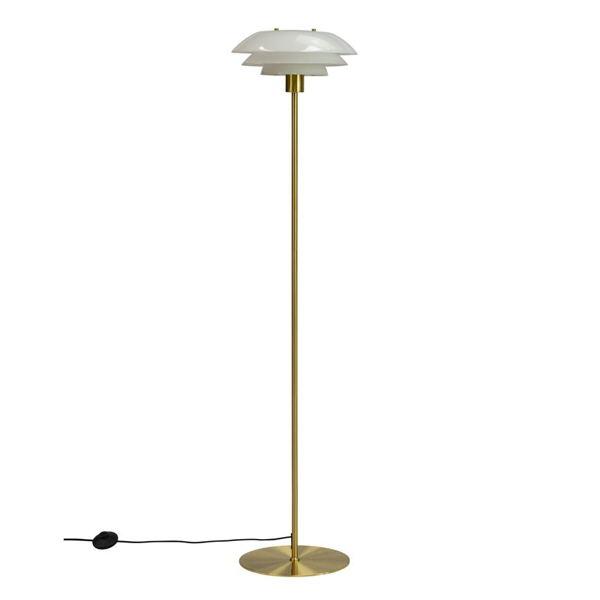Gulvlampe står på rund messingfod, med slank messingstang og trelags hvid skærm; ledning med sort fodkontakt ligger på hvid baggrund.