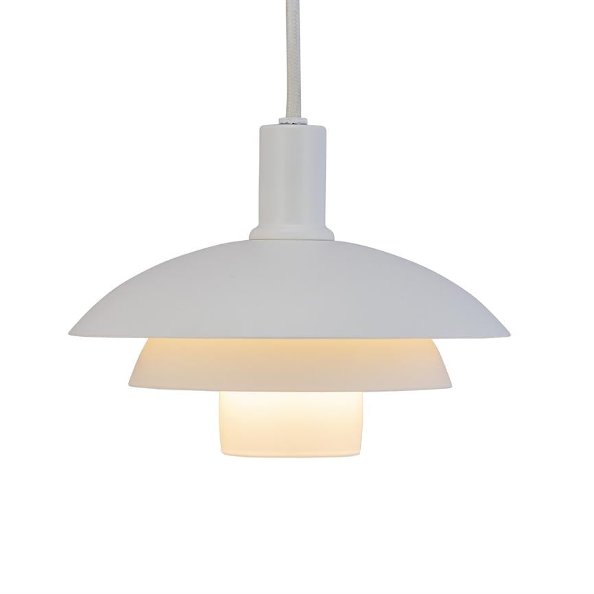 Hvid, flerlags pendel-lampe med tre skærme hænger i stofledning og udsender varmt, blødt lys mod en neutral, hvid baggrund.