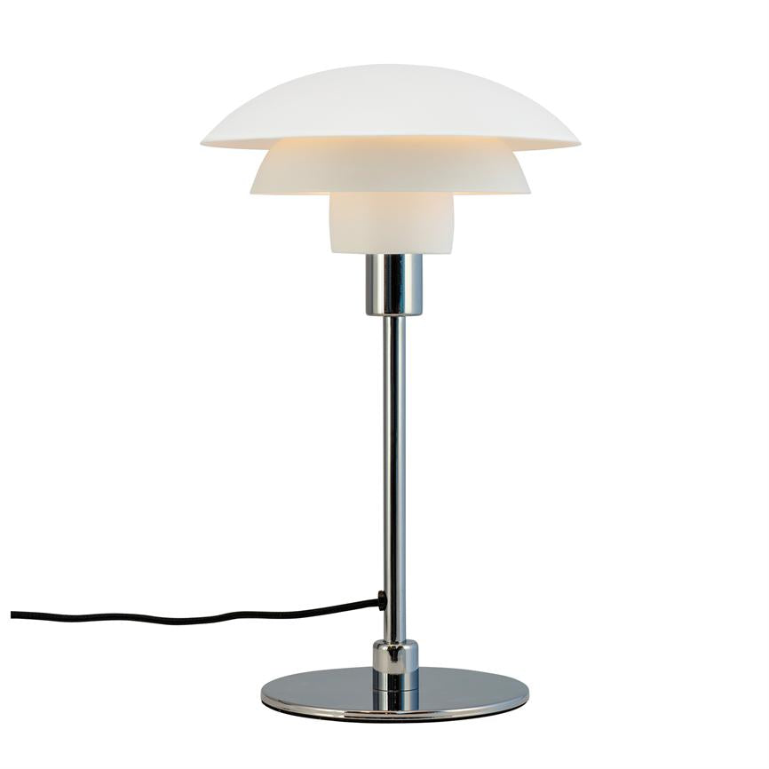 Bordlampe lyser blødt fra lagdelt, hvide skærme; slank kromstang og rund kromfod står på hvid baggrund, sort ledning løber ud til siden.