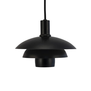 En sort pendel-lampe hænger i en sort stofledning over en neutral hvid baggrund; den har tre tierede, diskformede matte skærme i et moderne, minimalistisk design.