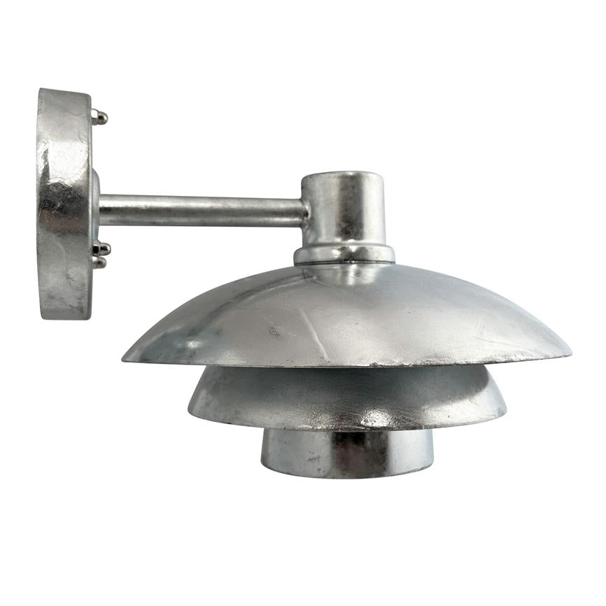 Sølvfarvet metalvæglampe med tre lagdelte, runde skærme er monteret på en kort arm og peger nedad mod en neutral hvid baggrund.
